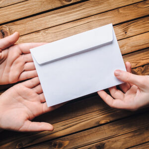 Hand pass the white envelope to the other hands on a wooden background. Transfer of money for donation. To send a letter. Hand pass the white envelope to the other hands on a wooden background. Transfer of money for donation. To send a letter.